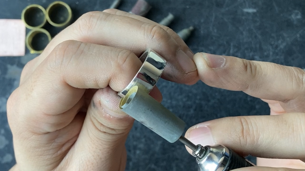 紙やすりを装着したリューターでシルバーリングの表面を研磨し、傷消しを行っている彫金作業の様子。ハンドメイドジュエリー制作における仕上げ工程。