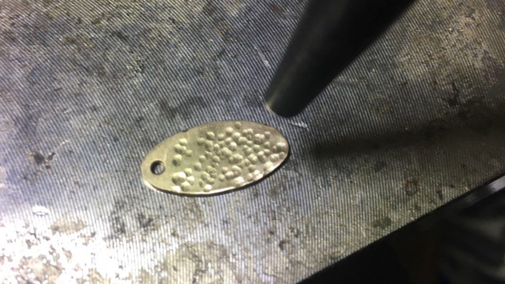 穴を開けた真鍮板に芋槌で槌目模様を打っていく