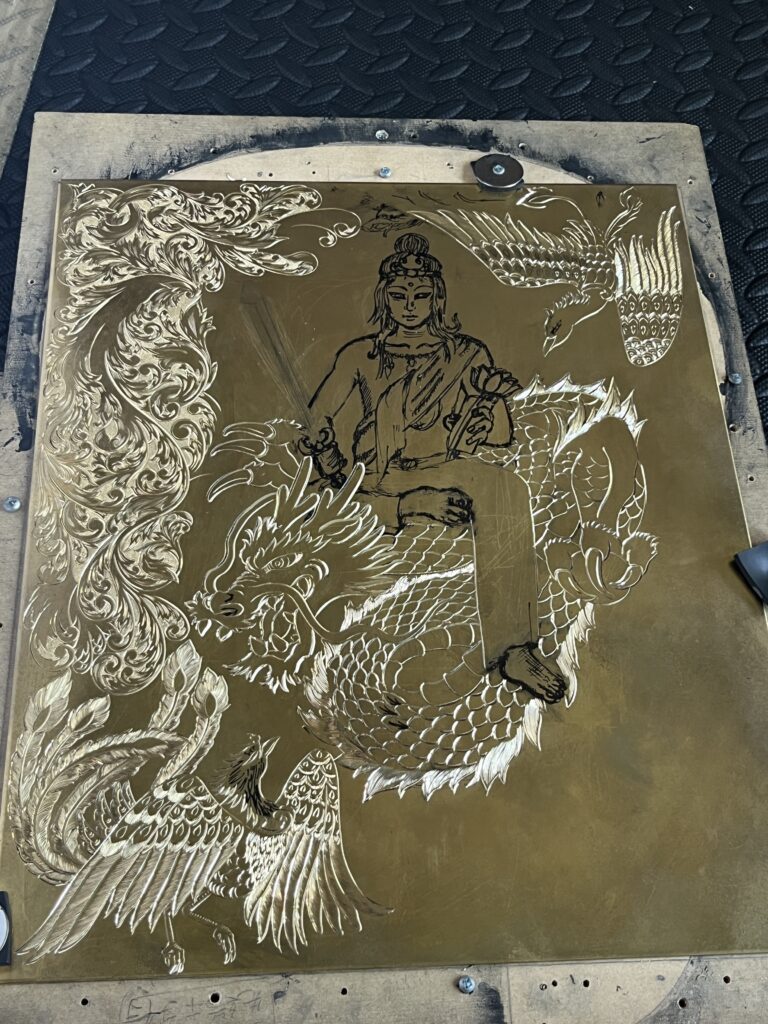 金属板に彫金で描かれた文殊菩薩の下絵。雲を纏った龍に乗る文殊菩薩を中心に、左右には翼を広げた鳳凰、周囲には唐草模様が緻密に彫り込まれている制作途中の図案。