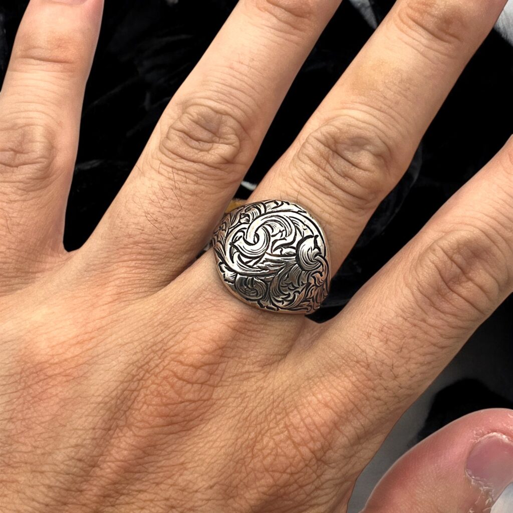 シルバーリングの着用写真。丸みを帯びたフェイス全面に唐草模様をエングレービングで彫金し、繊細な装飾と存在感を持つデザインを映したイメージ。