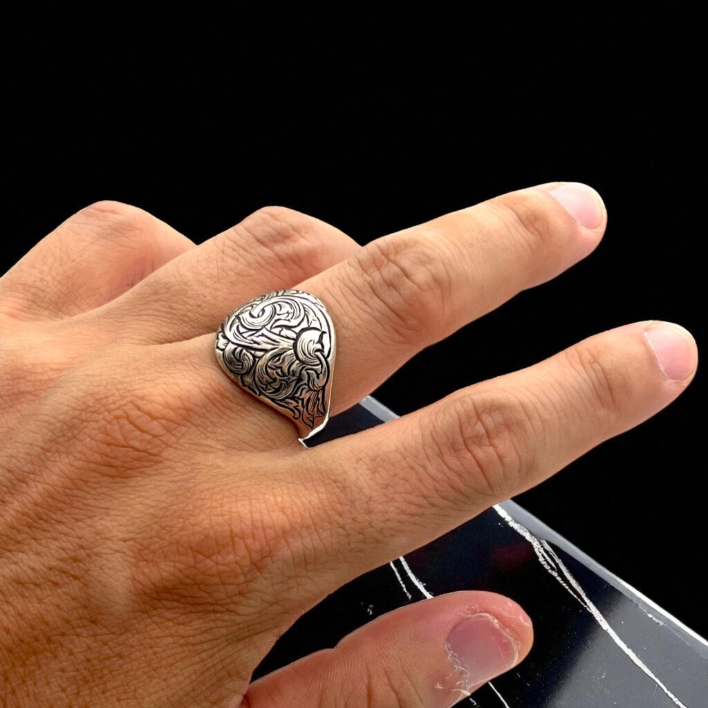男性の手に着用された唐草模様の手彫りシルバーリング。リングの立体的な彫金模様と燻し仕上げが指元に映える様子
